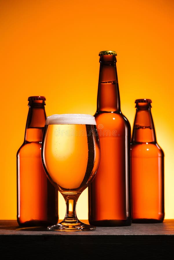 close up view of bottles and glass of beer with foam on surface