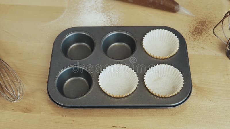 Close-up view of female hand putting the paper cups into the baking tray. Woman cooking cupcakes. Time lapse.