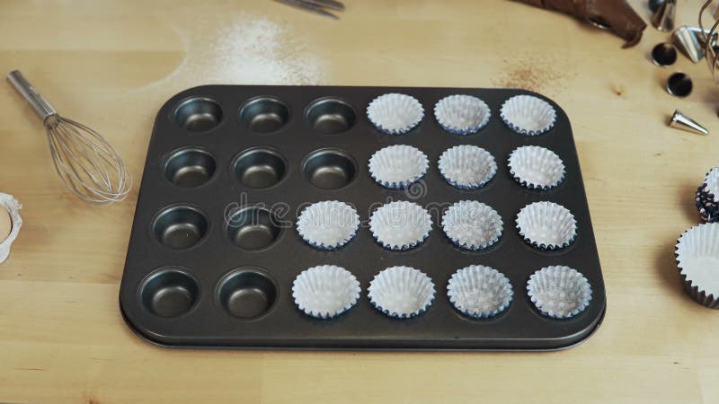 Close-up view of female hand putting the wrappers paper cups into the baking dish. Woman cooking cupcakes. Time lapse.
