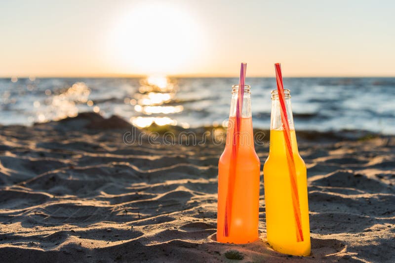 close-up view of glass bottles with refreshing beverages and drinking straws on sandy beach