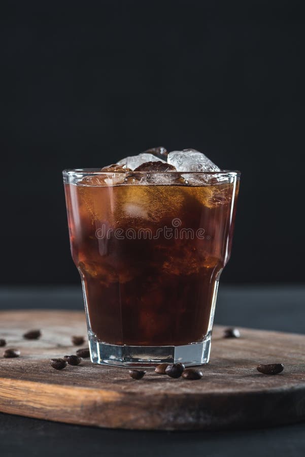 Close up view of glass of cold brewed coffee with roasted coffee beans on wooden cutting board stock image