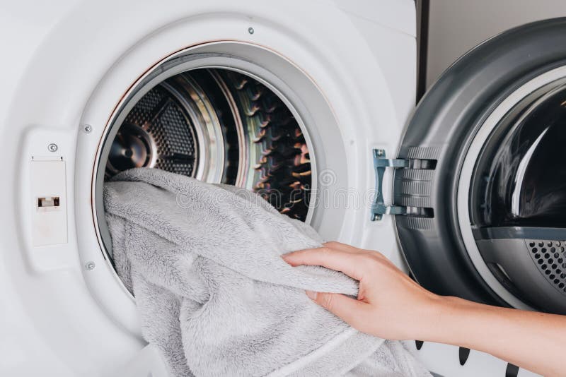 A Close-Up View of a Hand Loading a Soft Towel into a Modern Washing Machine for Effective Cleaning and Fabric Care royalty free stock image