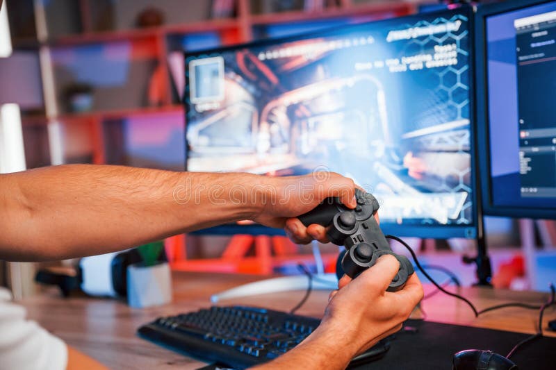 Close up view of hands with joystick controller. Male game streamer in casual clothes is indoors with pc