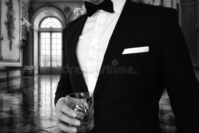 A close up view of a man in a black tuxedo holding a whiskey glass in a mansion. Great for use for a themed black tie event such stock image
