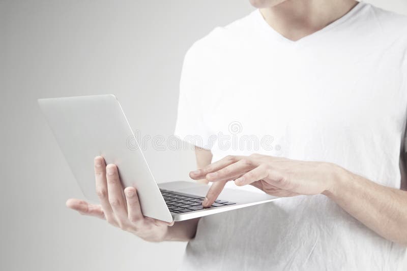 Close-up view of modern laptop in man`s hands, guy wearing white t-shirt, working on portable computer. White background in studio