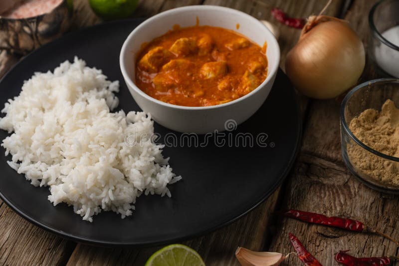 Close-up view of plate with classic chicken curry and rice served with lime and spices on rustic wooden table background. Traditional indian cuisine. Restaurant recipe.