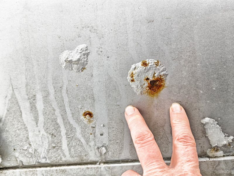 Close-up view of rust spots and corrosion on car body panel with human hand pointing at damage stock photos