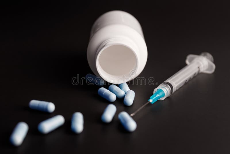 Close up view of a syringe with hypodermic needle and generic blue pills