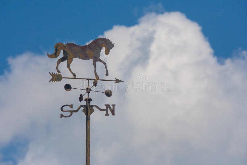 Close up weather vane or wind direction indicator on rooftop of house with blue sky in the background at countryside. stock photo Close up weather vane or wind direction indicator on rooftop of house with blue sky in the background at countryside. stock photo