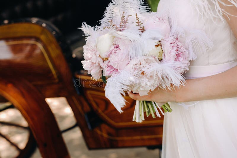 Close-up of a wedding bouquet of roses decorated with white feathers in the hands of the bride royalty free stock images