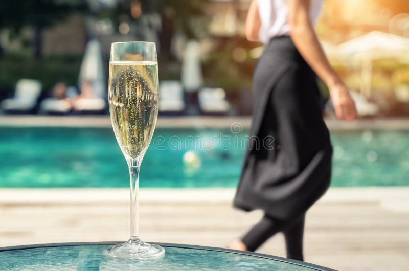 Close-up white champagne or prosecco glass against poolside at luxury resort hotel during vacation. Sparkling wine with rising