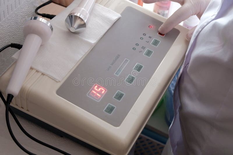 Close-up of a white-gloved hand pressing a power button on a digital ultrasonic massager device for skin. The concept of cosmetic