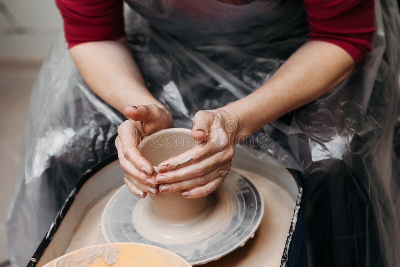 Close up of woman hands molding clay mug spinning on pottery wheel.