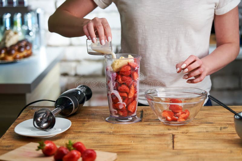 Close up of woman making strawberry smoothie. Healthy eating, cooking and summer refreshment concepts