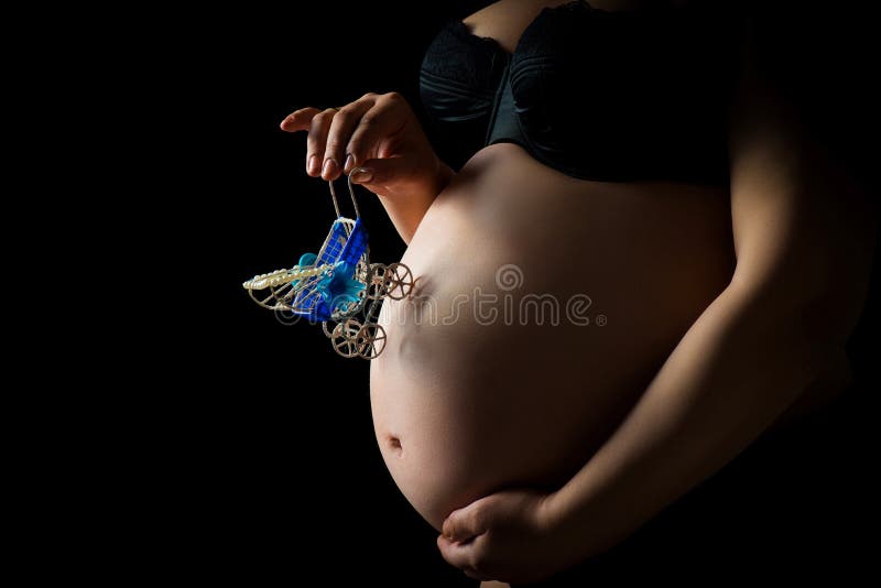 Close-up of woman pregnant belly with a toy pram. Girl tenderly holding her tummy with child. Concept of pregnancy, mother`s love