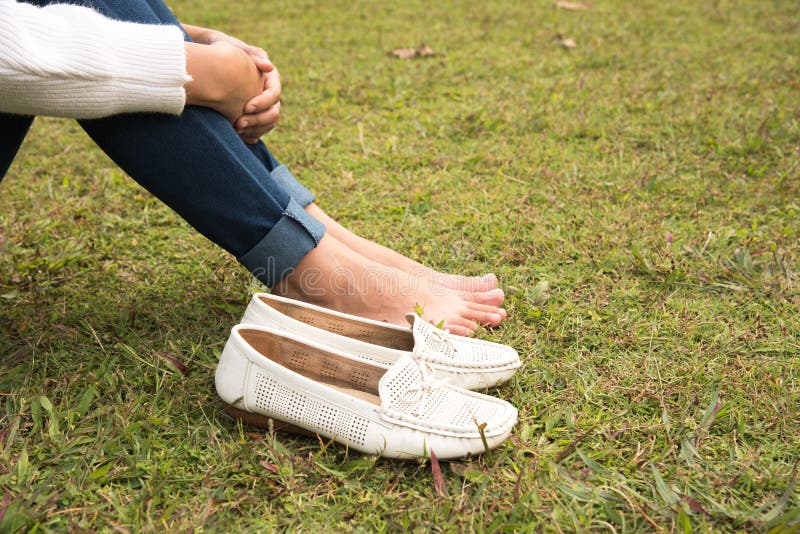 Close up Woman`s foot and white shoes sit on grass floor