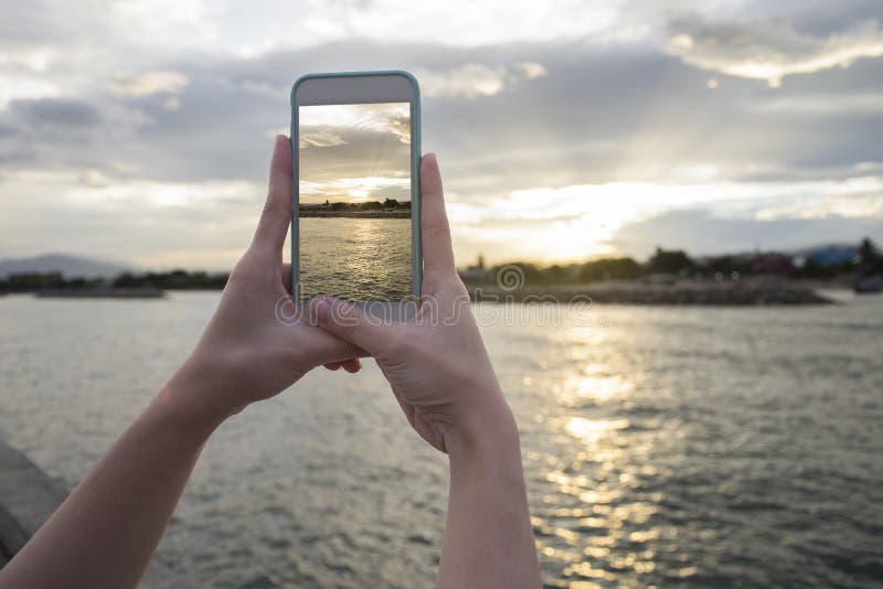 Close up of woman's hand holding smart phone, mobile, smart phone over blurred beautiful sea with sunset moment to take a pho stock photography Close up of woman's hand holding smart phone, mobile, smart phone over blurred beautiful sea with sunset moment to take a pho stock photography