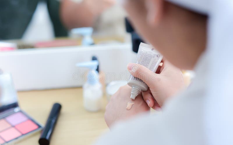 Close-up of a woman`s hand squeezing a tube of foundation cream from a tube onto the back of her hand to prepare her makeup.