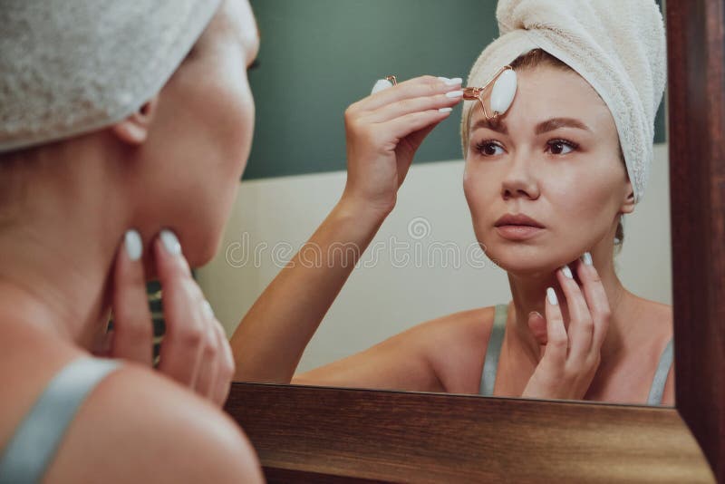 Close Up Woman Using Jade Facial Roller For Face Massage Looking In The