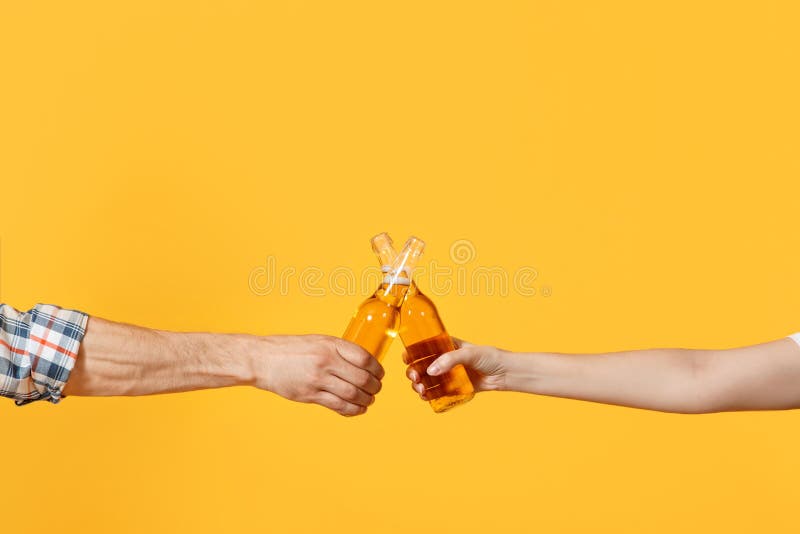 Close up of women and men hands horizontal holding beer bottles and clinking isolated on yellow background. Sport fans cheer up support team. Sport family leisure lifestyle concept. Close up of women and men hands horizontal holding beer bottles and clinking isolated on yellow background. Sport fans cheer up support team. Sport family leisure lifestyle concept