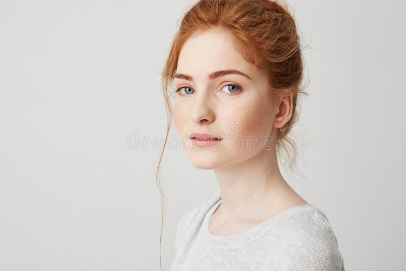 Close up of young tender beautiful ginger girl with blue eyes looking at camera over white background. Copy space.
