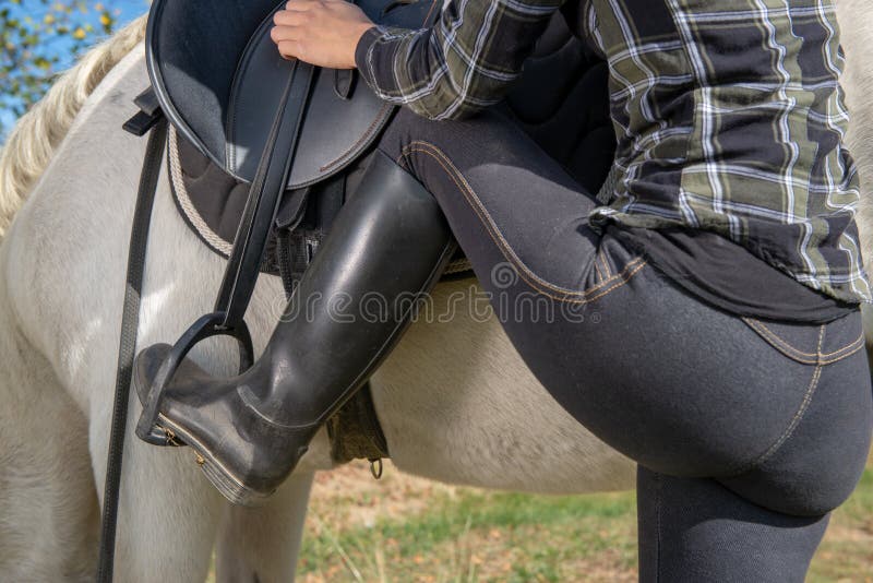 Close up of young woman rider mounting a white horse