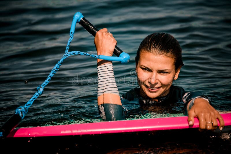 Close-up of young woman in wetsuit in water with surf style wakeboard and holding rope