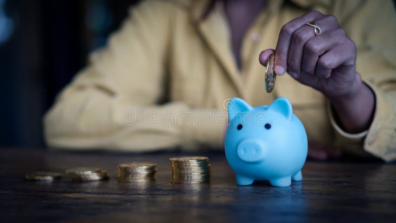 Close up young women put coins into a blue piggy bank sitting at a desk finance health insurance health money saving stock photography Close up young women put coins into a blue piggy bank sitting at a desk finance health insurance health money saving stock photography