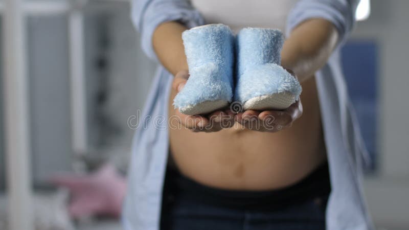 Close-up zwangere vrouwelijke handen die babyschoenen tonen