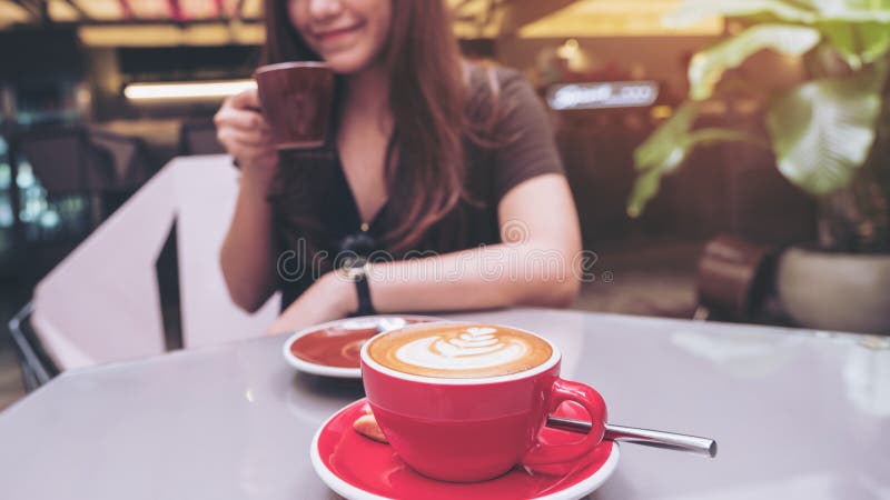 Close-upbeeld van een mooie Aziatische vrouw holding en het drinken koffie met de kop van de lattekoffie op glaslijst stock foto Close-upbeeld van een mooie Aziatische vrouw holding en het drinken koffie met de kop van de lattekoffie op glaslijst stock foto