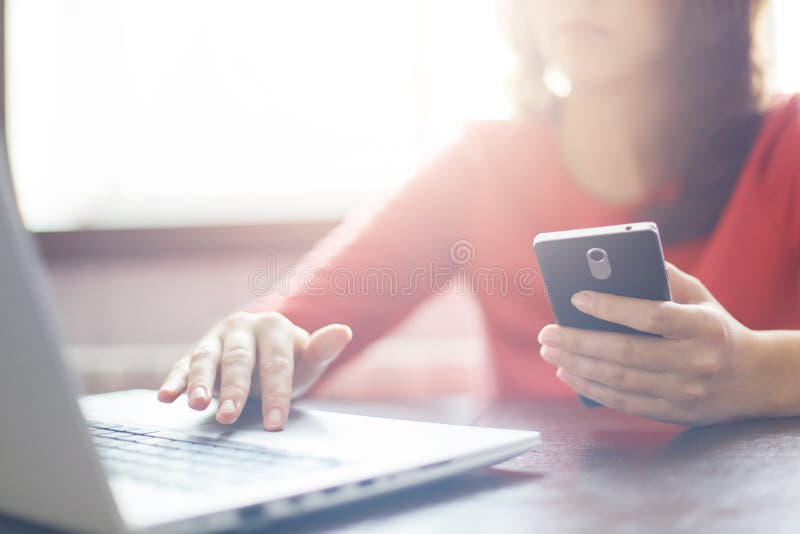 Close-upbeeld van vrouwen` s handen die smartphone houden en iets typen bij toetsenbord van laptop Jonge vrouwelijke het zoeken i royalty-vrije stock fotografie Close-upbeeld van vrouwen` s handen die smartphone houden en iets typen bij toetsenbord van laptop Jonge vrouwelijke het zoeken i royalty-vrije stock fotografie