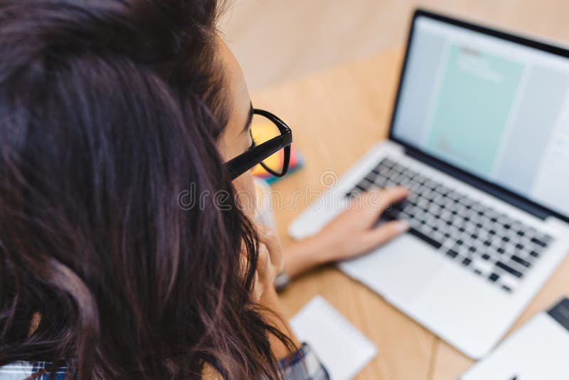 Close-upportret van achter donkerbruine jonge vrouw in zwarte glazen die met laptop aan lijst werken Het surfen in Internet royalty-vrije stock foto's Close-upportret van achter donkerbruine jonge vrouw in zwarte glazen die met laptop aan lijst werken Het surfen in Internet royalty-vrije stock foto's