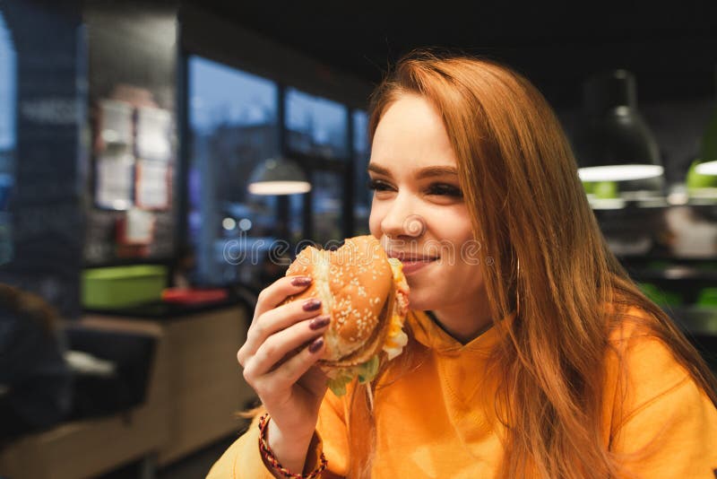 Close-upportret van een meisje die een grote smakelijke hamburger in haar hand en het lachen houden royalty-vrije stock afbeelding Close-upportret van een meisje die een grote smakelijke hamburger in haar hand en het lachen houden royalty-vrije stock afbeelding