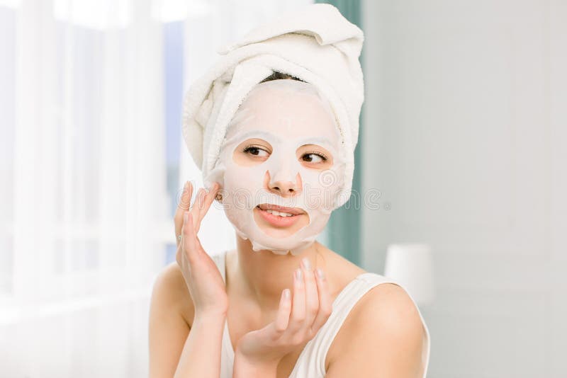 Closeup portrait of young pretty woman applying paper sheet mask on her face. Cosmetic procedure. Beauty spa and cosmetology. Closeup portrait of young pretty woman applying paper sheet mask on her face. Cosmetic procedure. Beauty spa and cosmetology