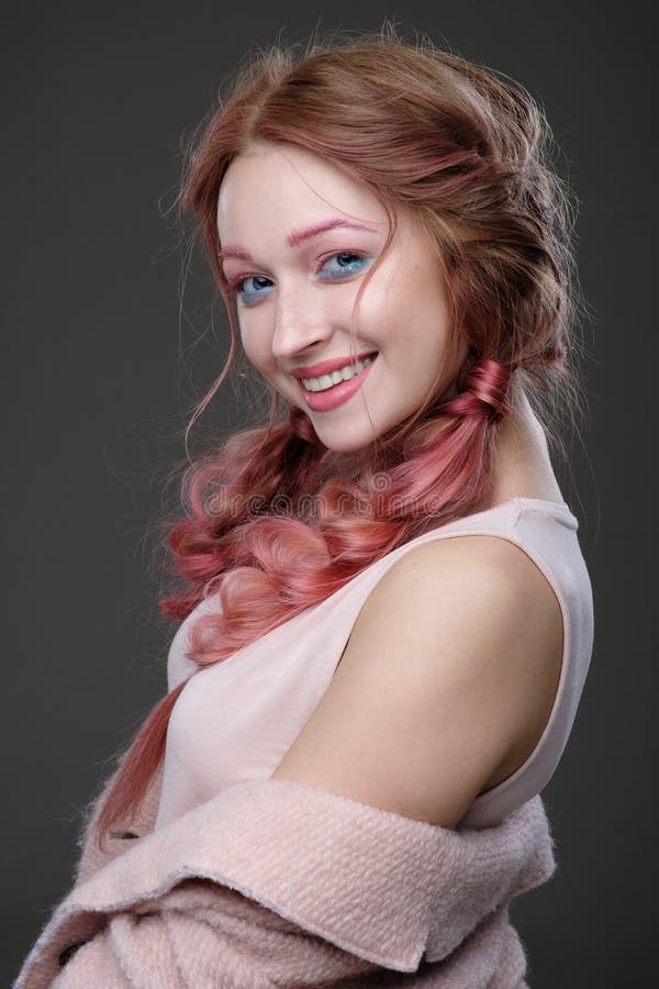 Close-upportret van meisje met roze haar in vlechten, en roze-blauwe make-up met een roze laag versleten van de schouder die zich royalty-vrije stock foto Close-upportret van meisje met roze haar in vlechten, en roze-blauwe make-up met een roze laag versleten van de schouder die zich royalty-vrije stock foto