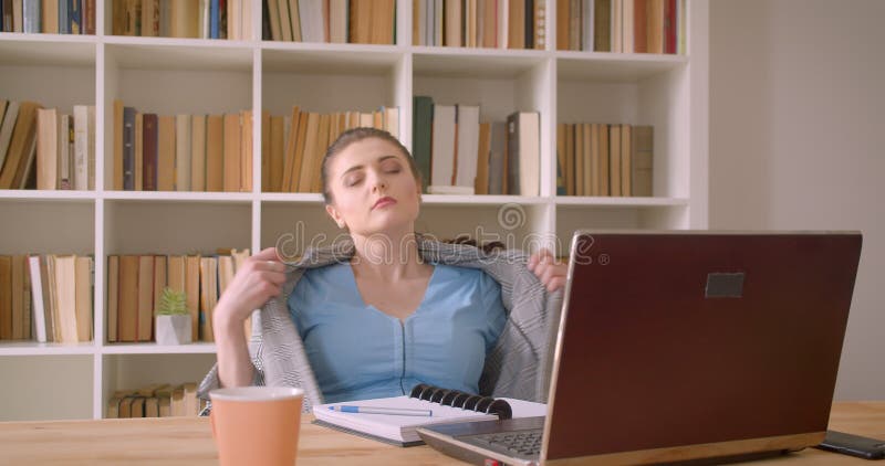 Close-upspruit van jonge Kaukasische onderneemster die laptop gertting gebruiken binnen heet en vermoeid in het bibliotheekbureau stock footage Close-upspruit van jonge Kaukasische onderneemster die laptop gertting gebruiken binnen heet en vermoeid in het bibliotheekbureau stock footage