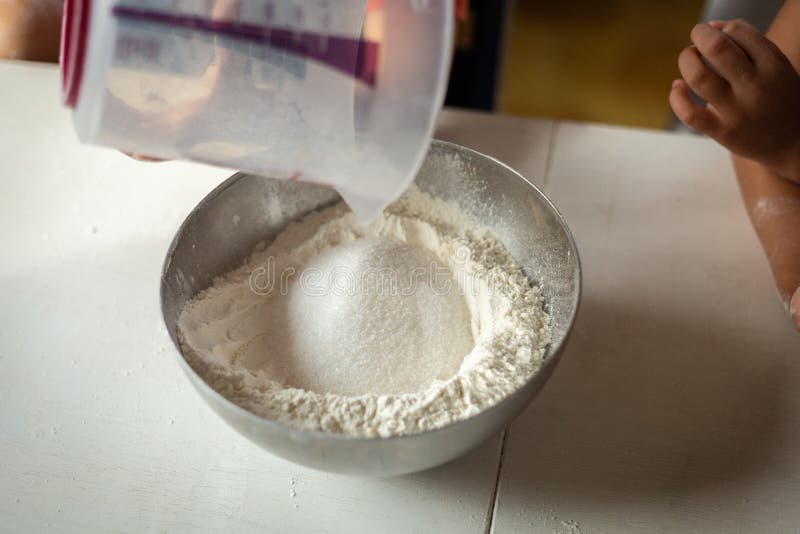 A close view of the hand of the child adding sugar to flour stock photos