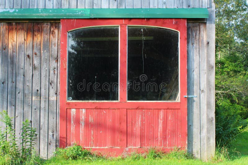 Close view of red barn doors on a weathered wood building with large windows and green door track