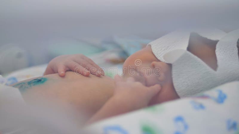 A close view on a sleeping and deeply breathing baby with attached tubing.