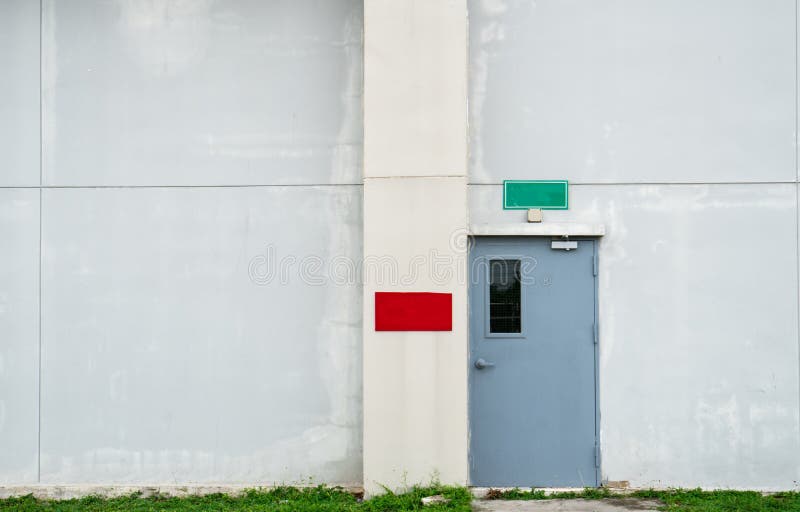 Closed grey door with green and red text box on white concrete wall