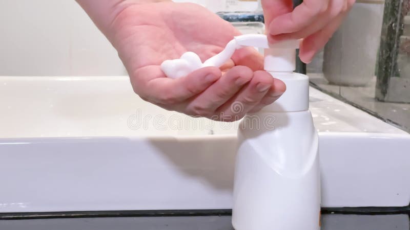 Closeudo d'une personne utilisant un distributeur de savon en mousse blanche dans un lavabo de salle de bain blanc. Capture de mou banque de vidéos