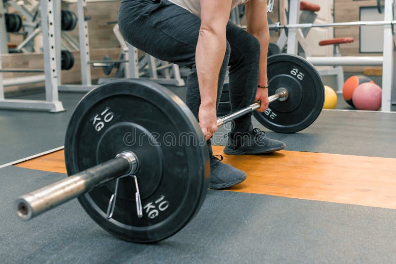 Closeup of arms and legs of man exercising with barbell at sport gym. Athlete, bodybuilding, training, weightlifting, workout exercises concept.