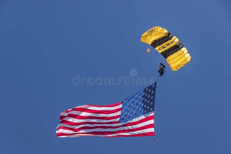 Santa Maria, CA, USA - June 6, 2010: Rodeo. Closeup of Yellow Army parachute descending with large US flag on foot in blue sky. Santa Maria, CA, USA - June 6, 2010: Rodeo. Closeup of Yellow Army parachute descending with large US flag on foot in blue sky