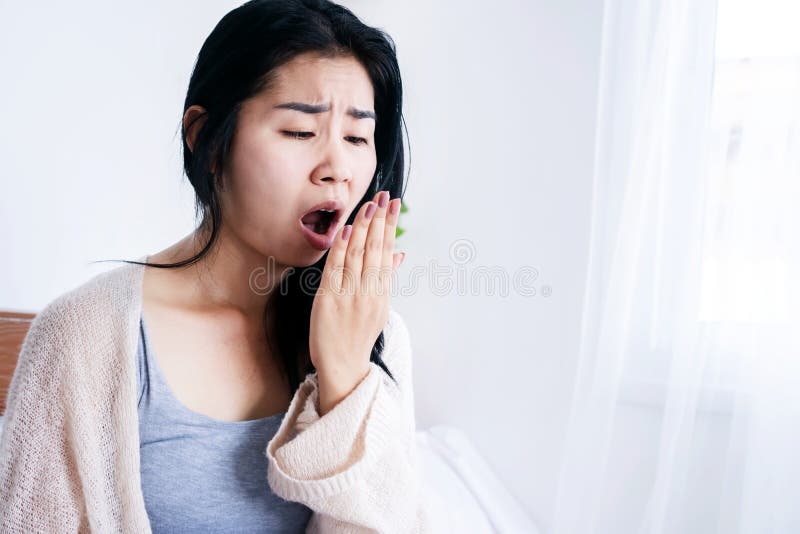 Asian woman sitting in bed open mouth checking her bad breath smell after wake up in the morning