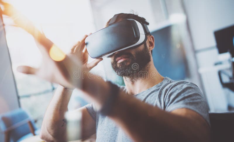 Closeup of bearded young man wearing virtual reality goggles in modern coworking studio. Smartphone using with VR