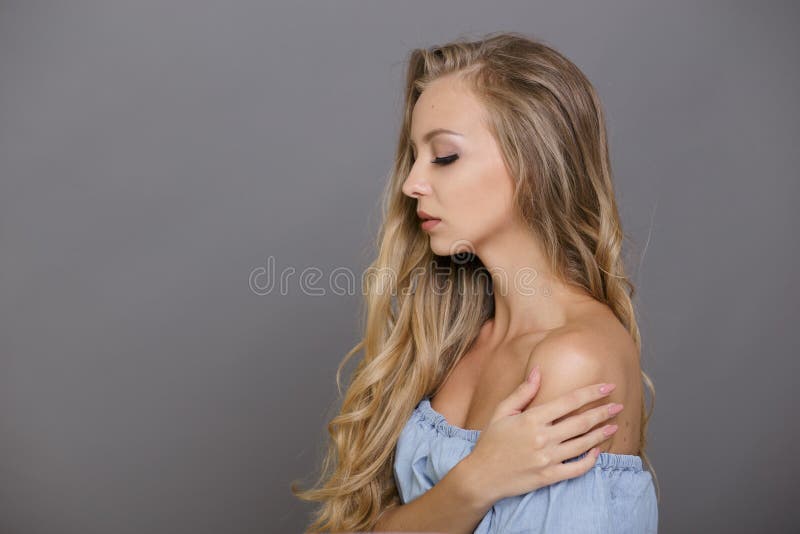 Closeup of beautiful blonde woman with closed eyes, posing in profile, touch gentle her shoulder, on grey background.