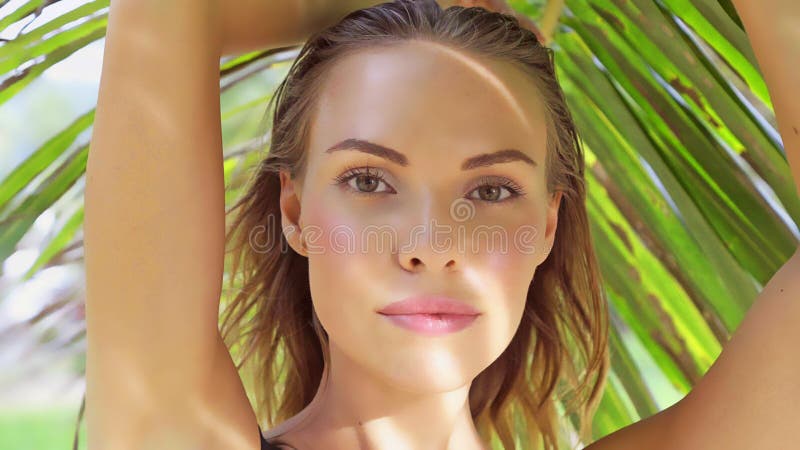 Closeup of beautiful glamour woman wearing black swimwear posing on a beautiful summer day between palm trees