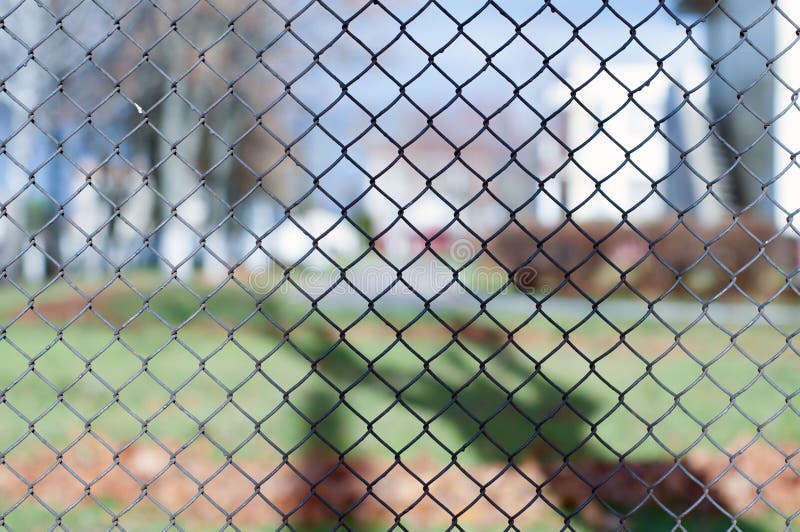 Closeup of black metal netting wire mesh fence against green field meadow. Texture pattern surface background of chain link wire-