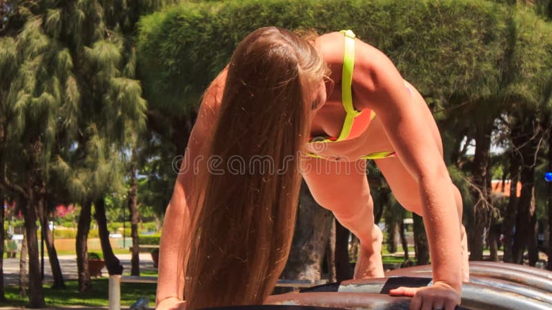 closeup blonde slim girl in bikini pushes up on arch ladder
