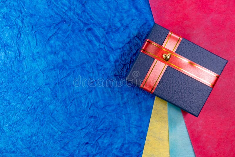 Closeup of a blue gift box with heart and red ribbons over color papers in background. Wives and husbands gifts concept royalty free stock photography